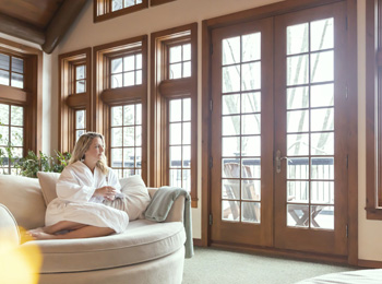 Woman in bathrobe sitting on a comfy chair in a room with many windows.