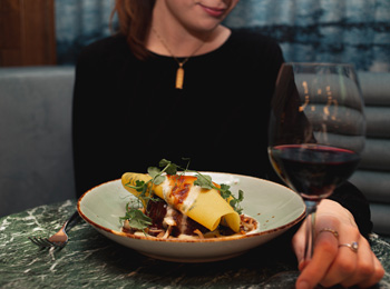 Gourmet pasta meal served with a glass of red wine; a woman is sitting the background.