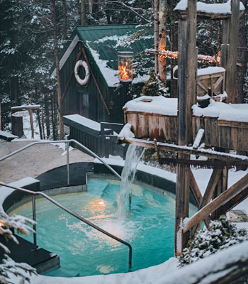 A thermal pool surrounded by snow and trees at dusk.