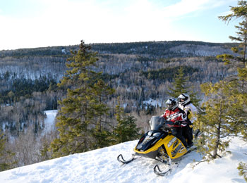 Two snowmobilers riding past mountains in the Mauricie region