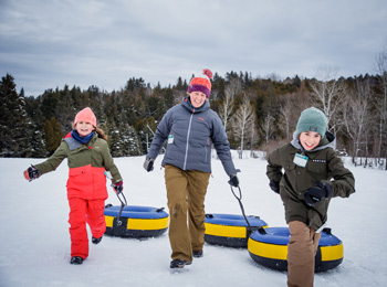 A woman and two children in snowsuits going snow tubing