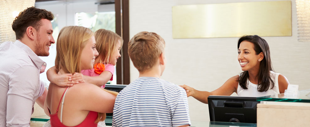 A young family at the front desk of a hotel, the receptionist is handing them something.