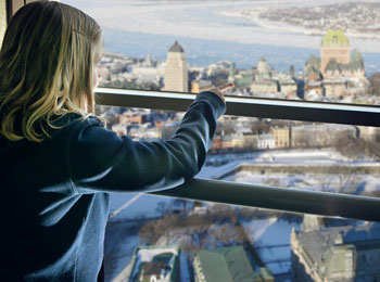 A young girl is standing in front of a window, pointing at the Château Frontenac in the distance
