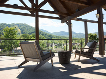 A covered outdoor terrace, featuring two comfortable chairs, overlooks a mountainous landscape.