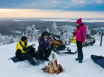 3 snowmobilers taking a break around the fire at the top of a mountain in the Laurentians