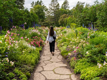 Woman walking on a stone path through a flower garden.