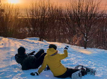 Two snowshoeing enthusiasts sit on the snow to watch the setting sun