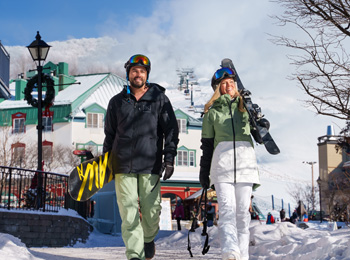 A man and a woman walking with their skiing and snowboarding equipment in Tremblant